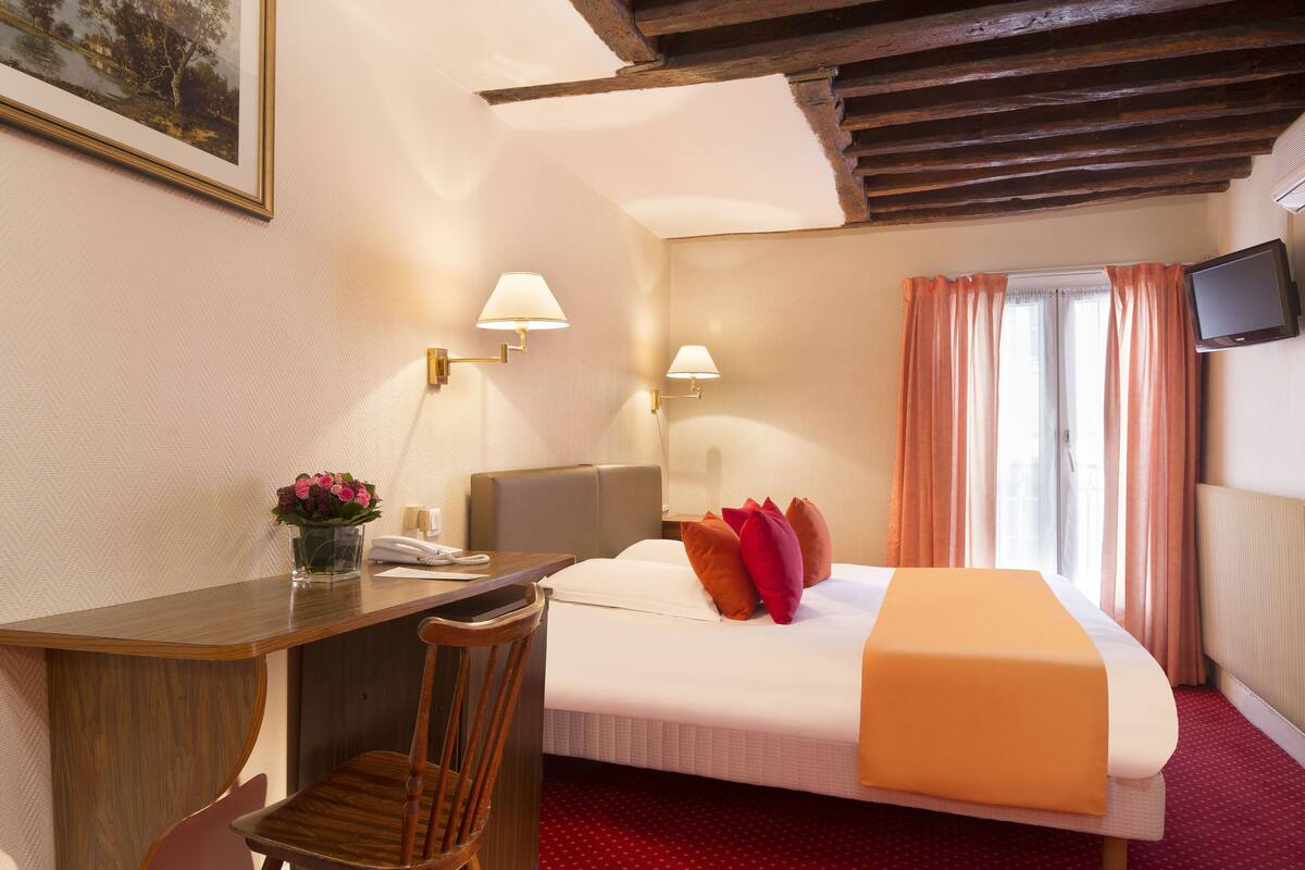 A hotel room with a bed, a desk, a chair, a TV, and a window with curtains.