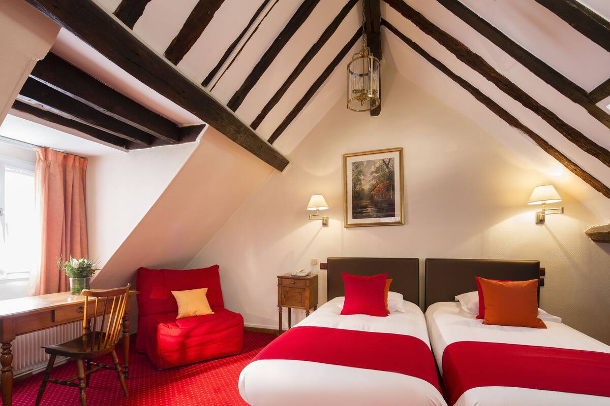A room with two beds, a desk, a chair, and a red sofa.