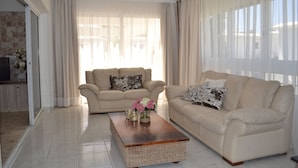 Una sala de estar con dos sofás color beige, una mesa de centro de madera y un ventanal con cortinas translúcidas.