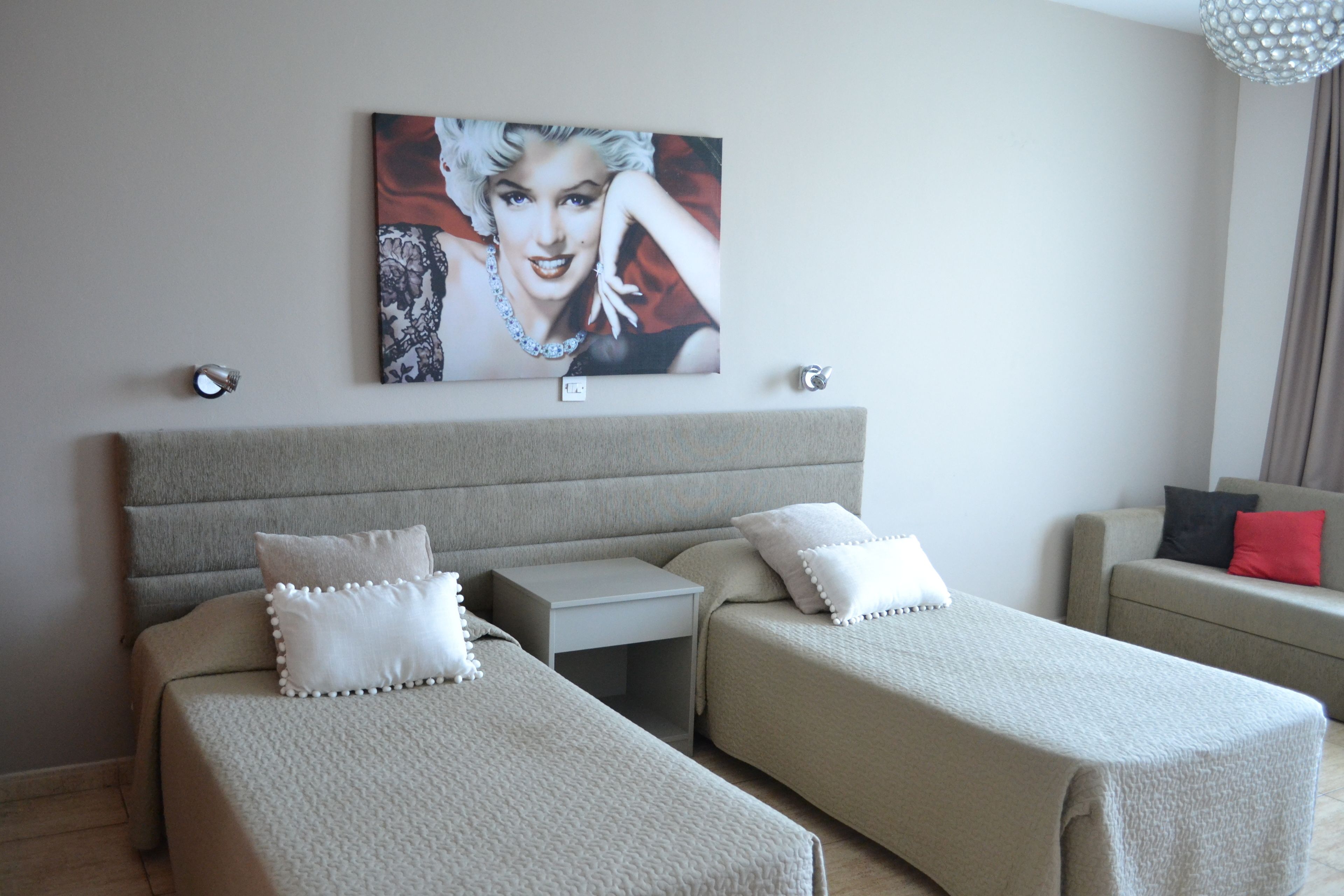 Une chambre d’hôtel avec deux lits simples, une table de chevet, une petite table, un canapé et un tableau au mur.