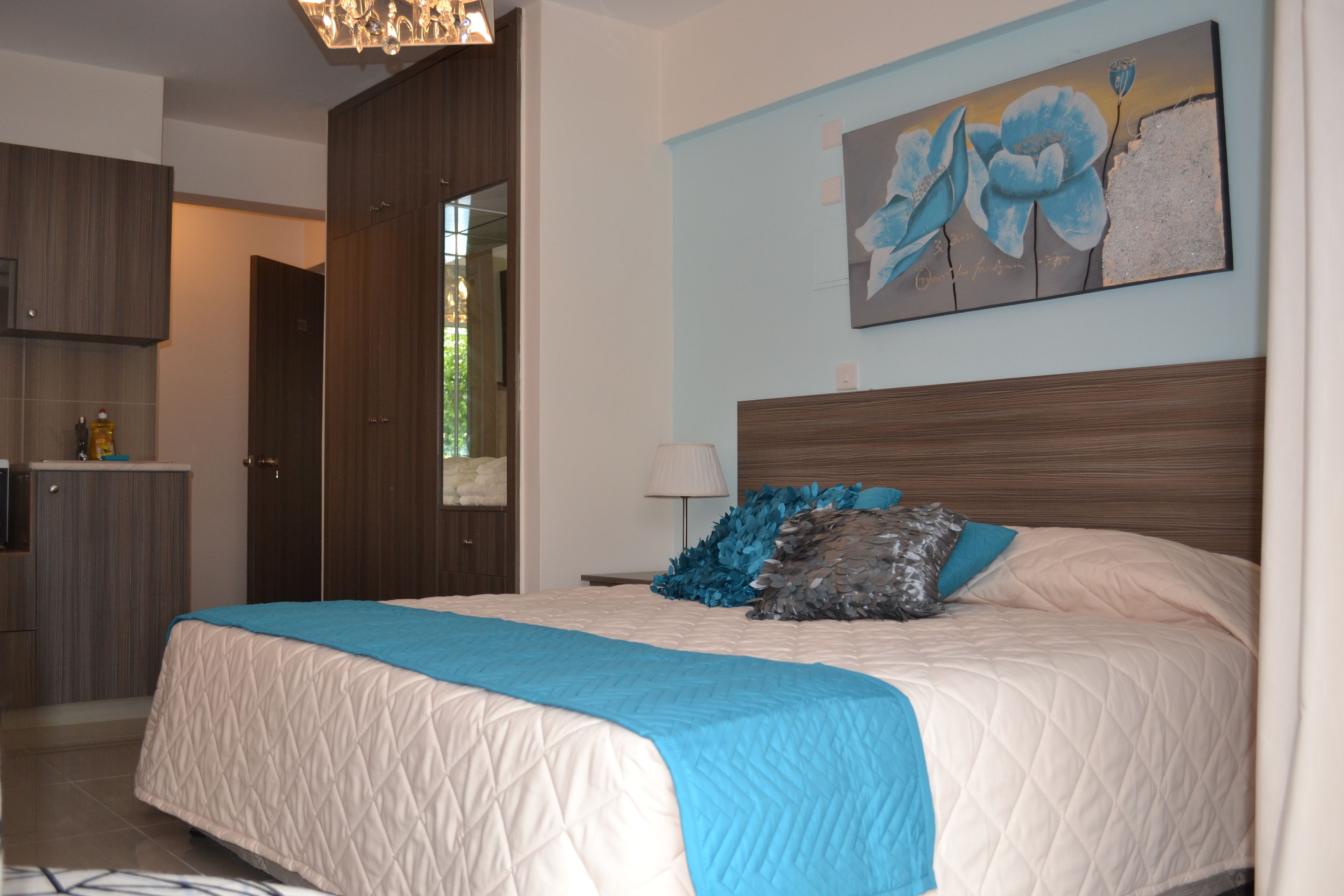 Un dormitorio con una cama grande, cabecera de madera, colcha acolchada azul y blanca, y un cuadro de flores en la pared.