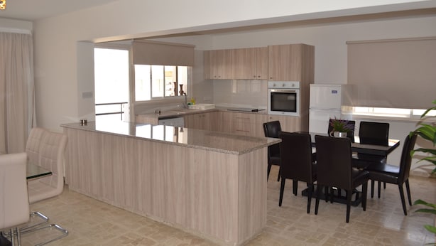 Una cocina moderna con una isla central, comedor con sillas y un refrigerador.