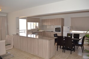 Una cocina moderna con una isla central, comedor con sillas y un refrigerador.