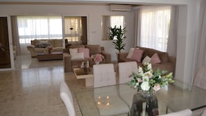 Un salón amplio con una mesa de centro de vidrio, sofás color beige y una planta grande en maceta.