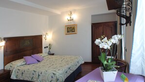 A bedroom with a bed, a nightstand, a table with a vase of flowers, and a door. - Hotel Centrale (Bellagio)