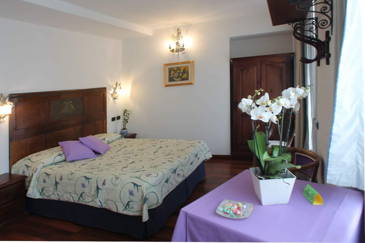 A bedroom with a bed, a nightstand, a table with a vase of flowers, and a door.
