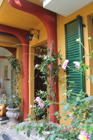 Traditional architecture with a red entrance, green shutters, and a potted plant.