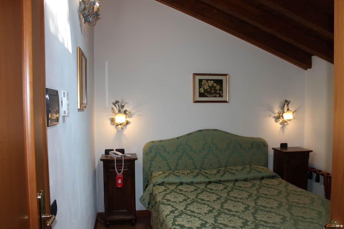 A bedroom with a bed, two wall-mounted lamps, a framed picture, and a wooden headboard.
