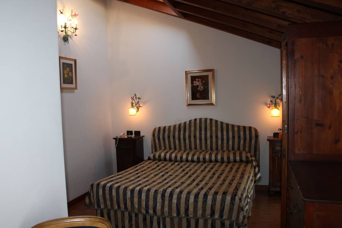 A bedroom with a striped bedspread, two wall-mounted lamps, and framed pictures on the walls.