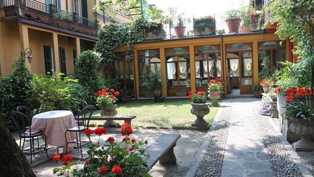 A courtyard with a table and chairs, potted plants, and a stone bench. - Hotel Centrale (Bellagio)
