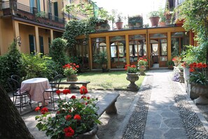 A courtyard with a table and chairs, potted plants, and a stone bench. - Hotel Centrale (Bellagio)