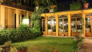 A courtyard with a yellow building, potted plants, and a glass-enclosed area. - Hotel Centrale (Bellagio)