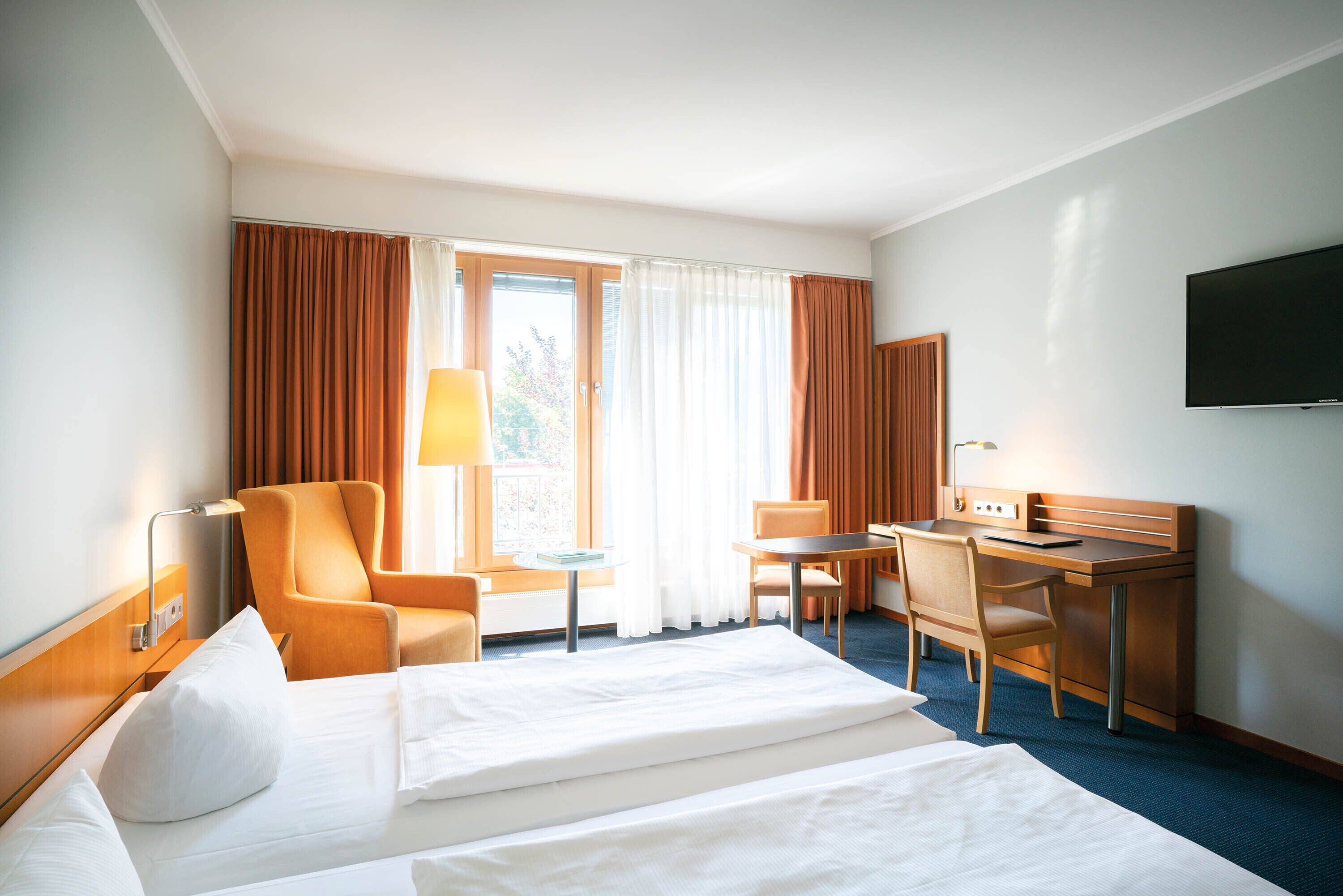 Habitación de hotel con cama, dos sillones, escritorio, televisor y ventana con cortinas.