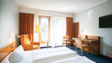 Habitación de hotel con cama, dos sillones, escritorio, televisor y ventana con cortinas.