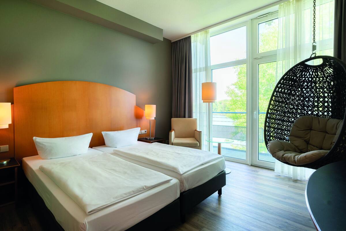A hotel room with two beds, a hanging chair, and large windows.