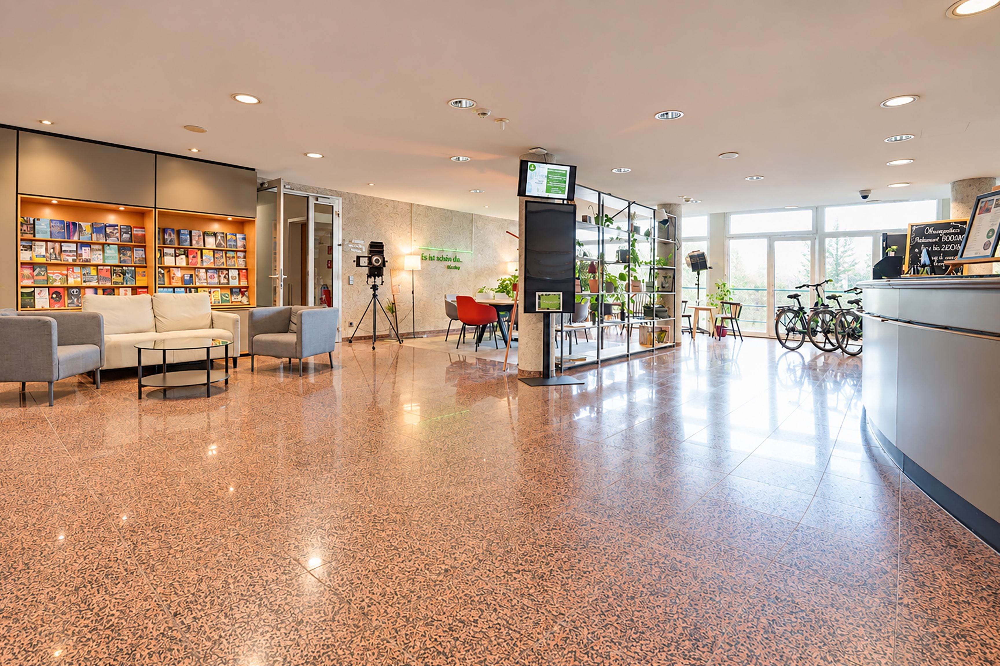 A spacious lobby with a polished floor, seating area, bookshelves, a reception desk, and bicycles.