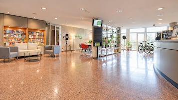 A spacious lobby with a polished floor, seating area, bookshelves, a reception desk, and bicycles.