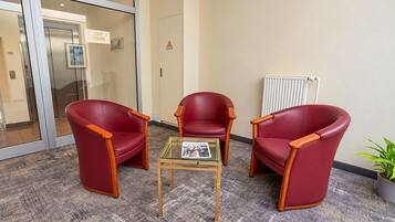 Une salle d’attente avec trois chaises rouges, une table à plateau en verre et un radiateur fixé au mur.