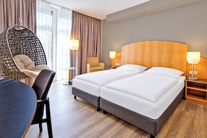 Una habitación de hotel con una cama, dos sillas, un sillón colgante y un escritorio.