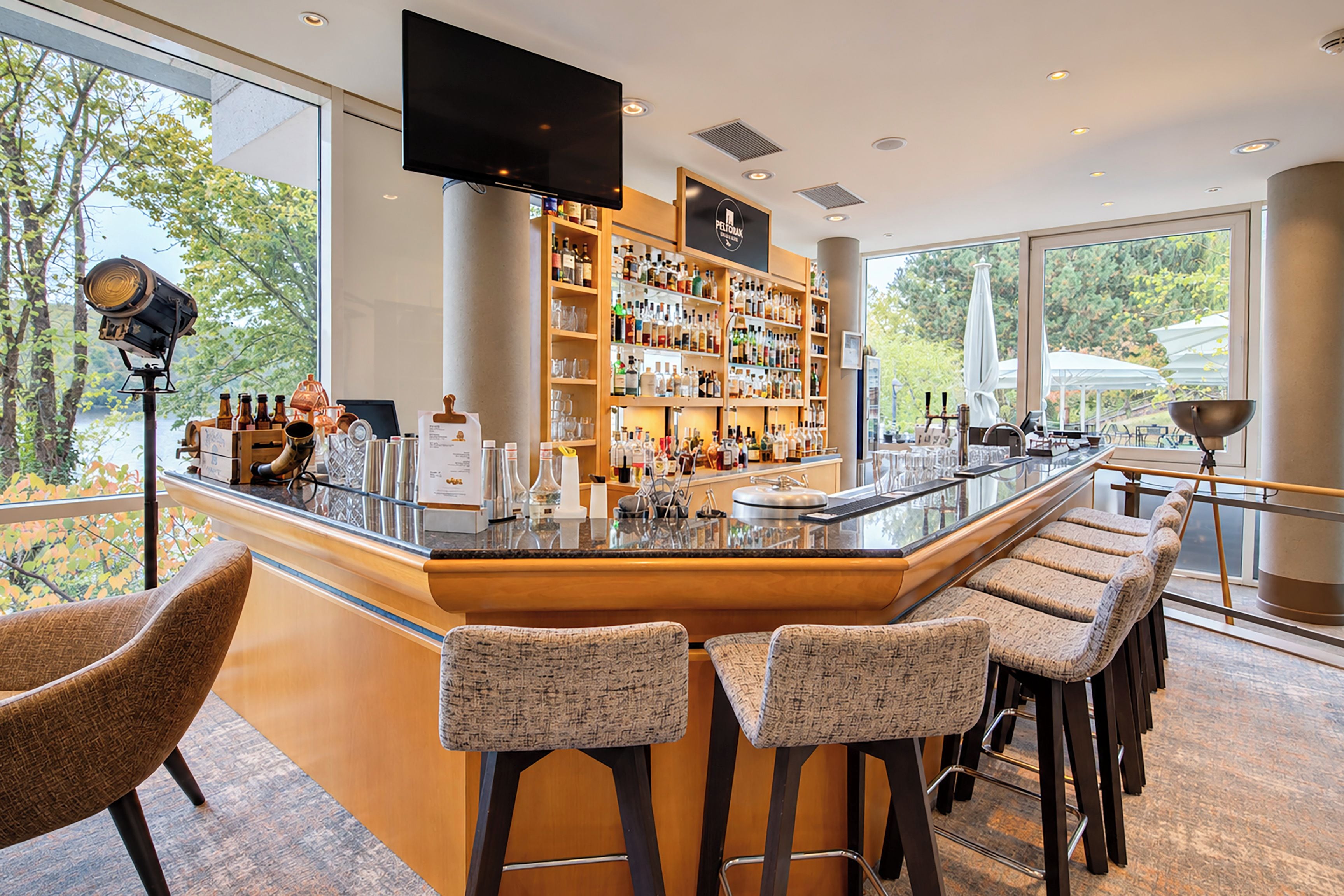 A modern bar area with a long counter, bar stools, and a television screen.