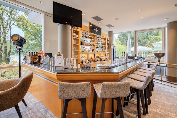 A modern bar area with a long counter, bar stools, and a television screen. - Seminaris Sunday Hotel Potsdam Babelsberg (Potsdam)