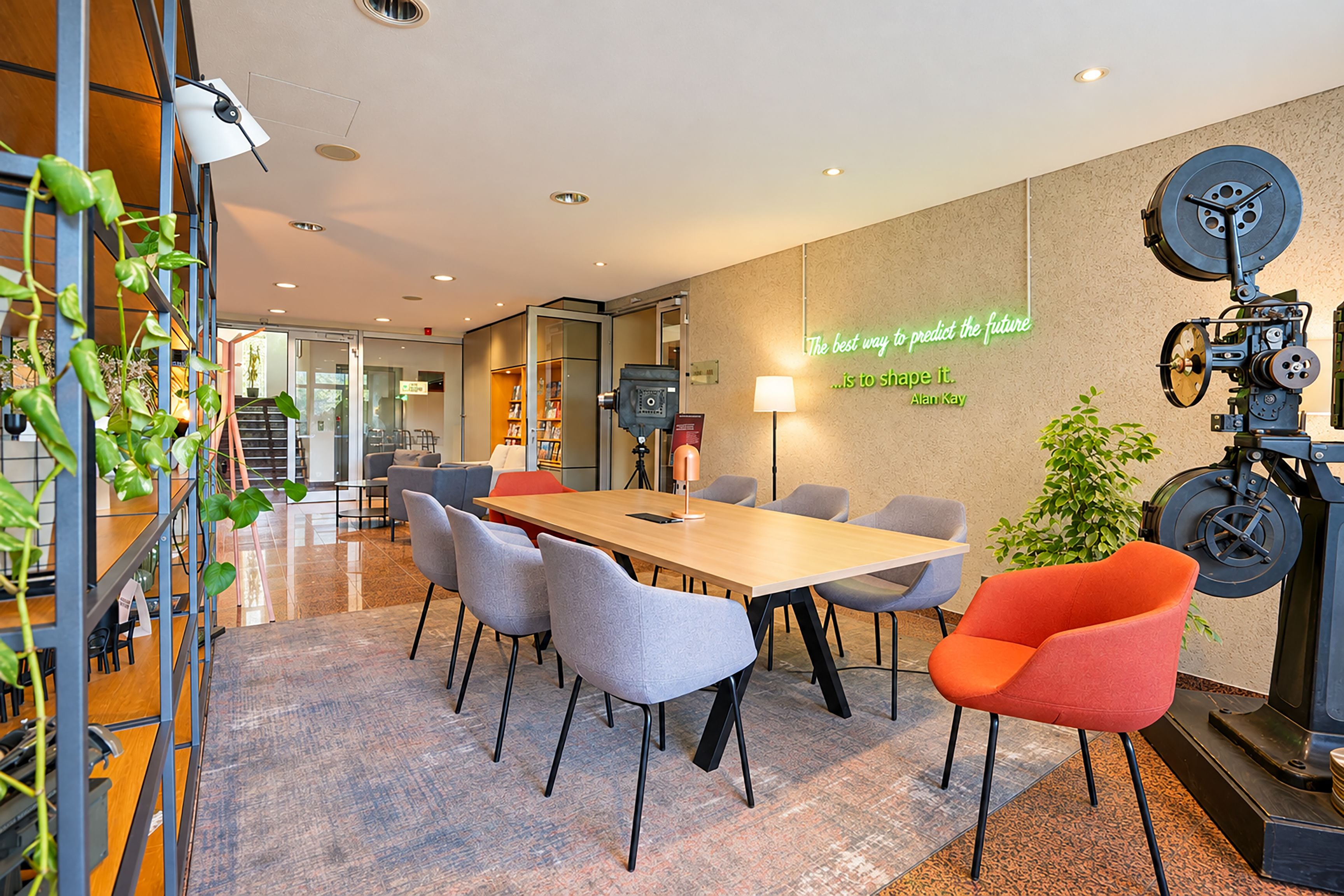 Un salón de conferencias moderno con una mesa larga, varias sillas, una frase iluminada con neón en la pared y un proyector antiguo.