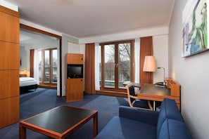 A hotel room with a bed, a desk, a sofa, a TV, and large windows. - Seminaris Sunday Hotel Potsdam Babelsberg (Potsdam)