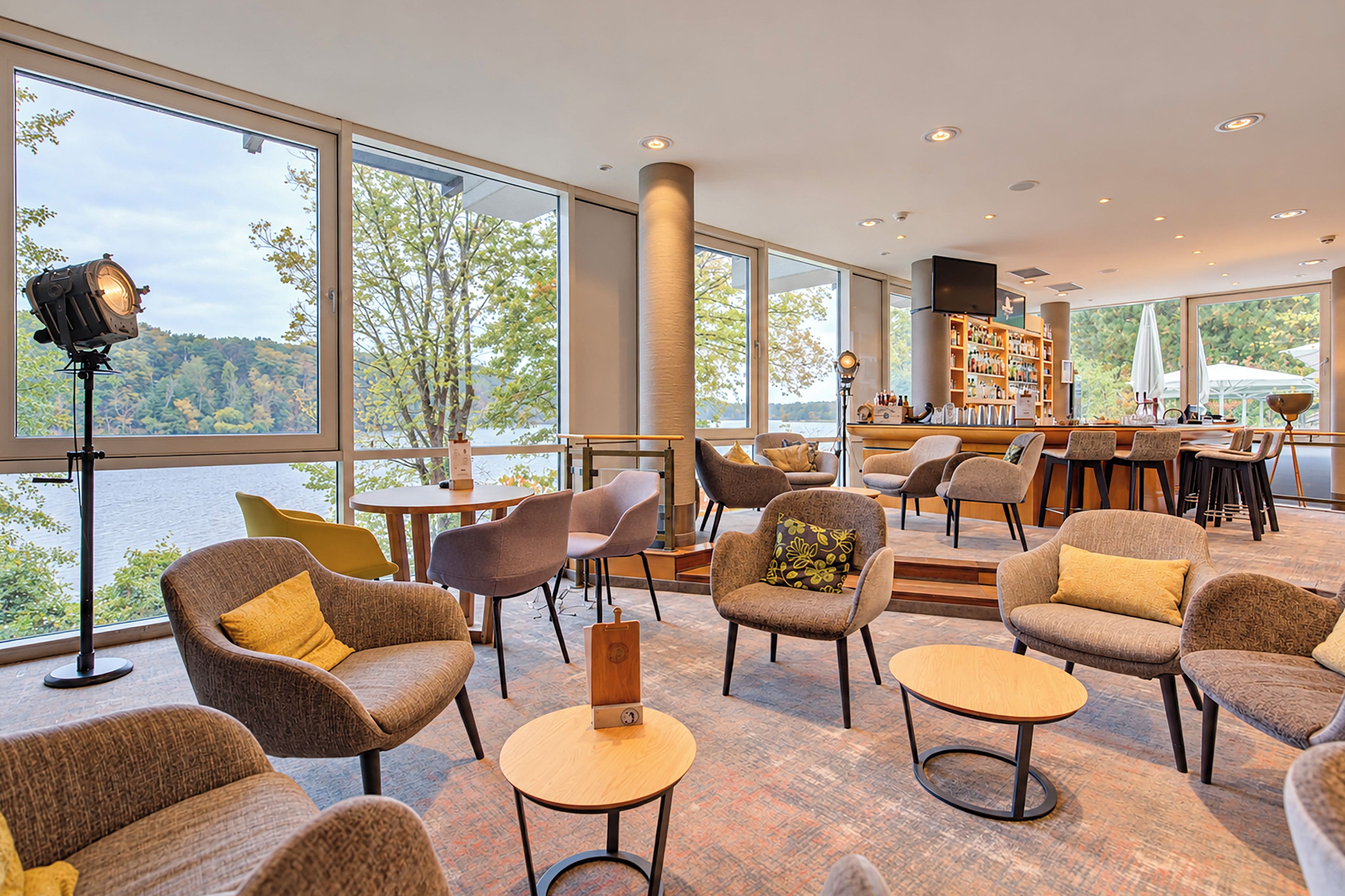 Ein großzügiger Lounge-Bereich mit verschiedenen Sitzmöglichkeiten, einer Bar und großen Fenstern mit Blick ins Freie.