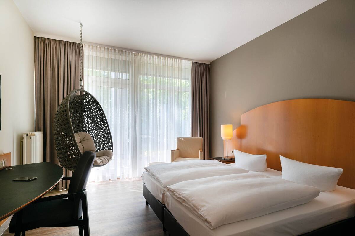 A hotel room with a bed, a desk, a chair, and a hanging chair.
