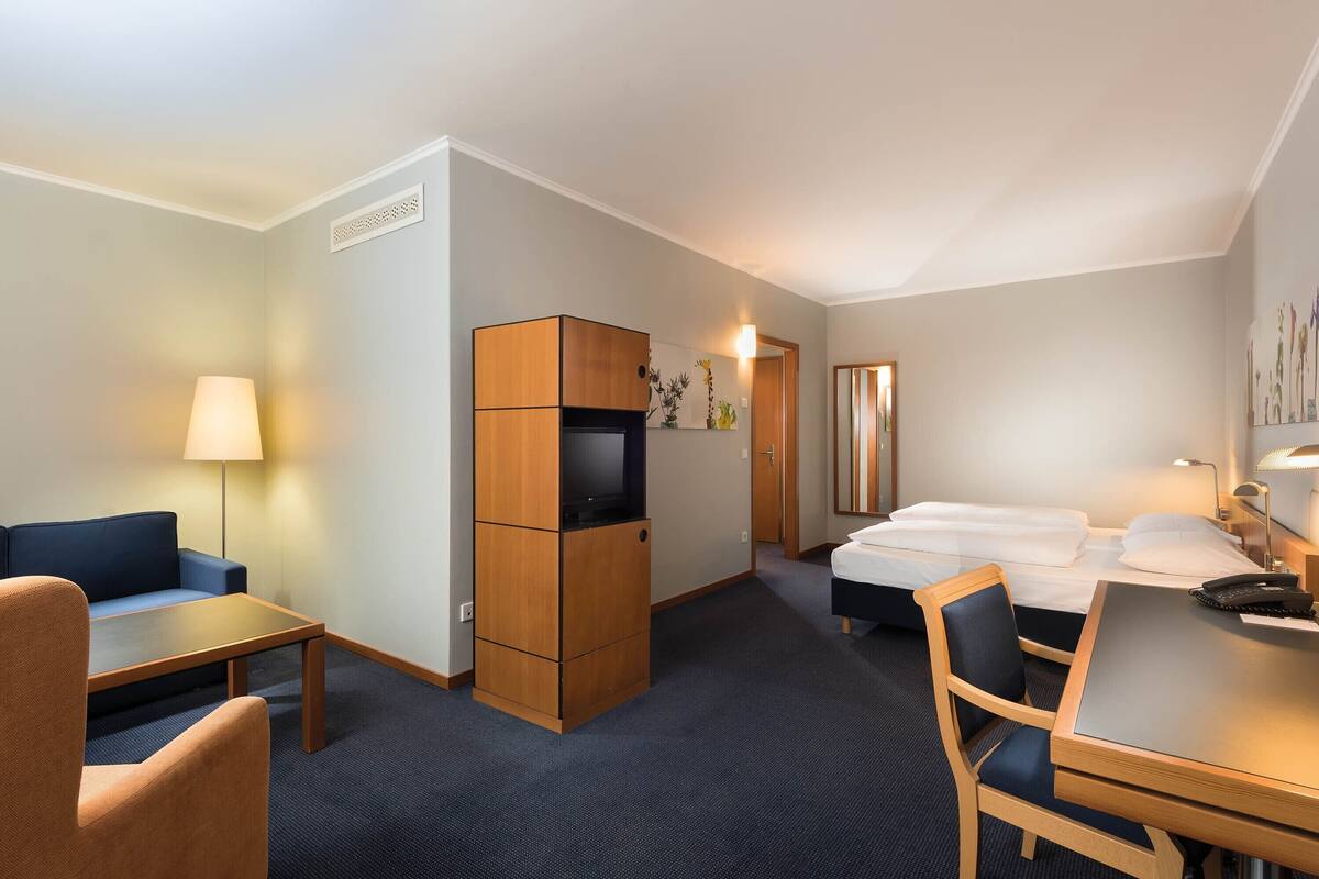 A hotel room with a sofa, a desk, a TV, a bed, and a nightstand.