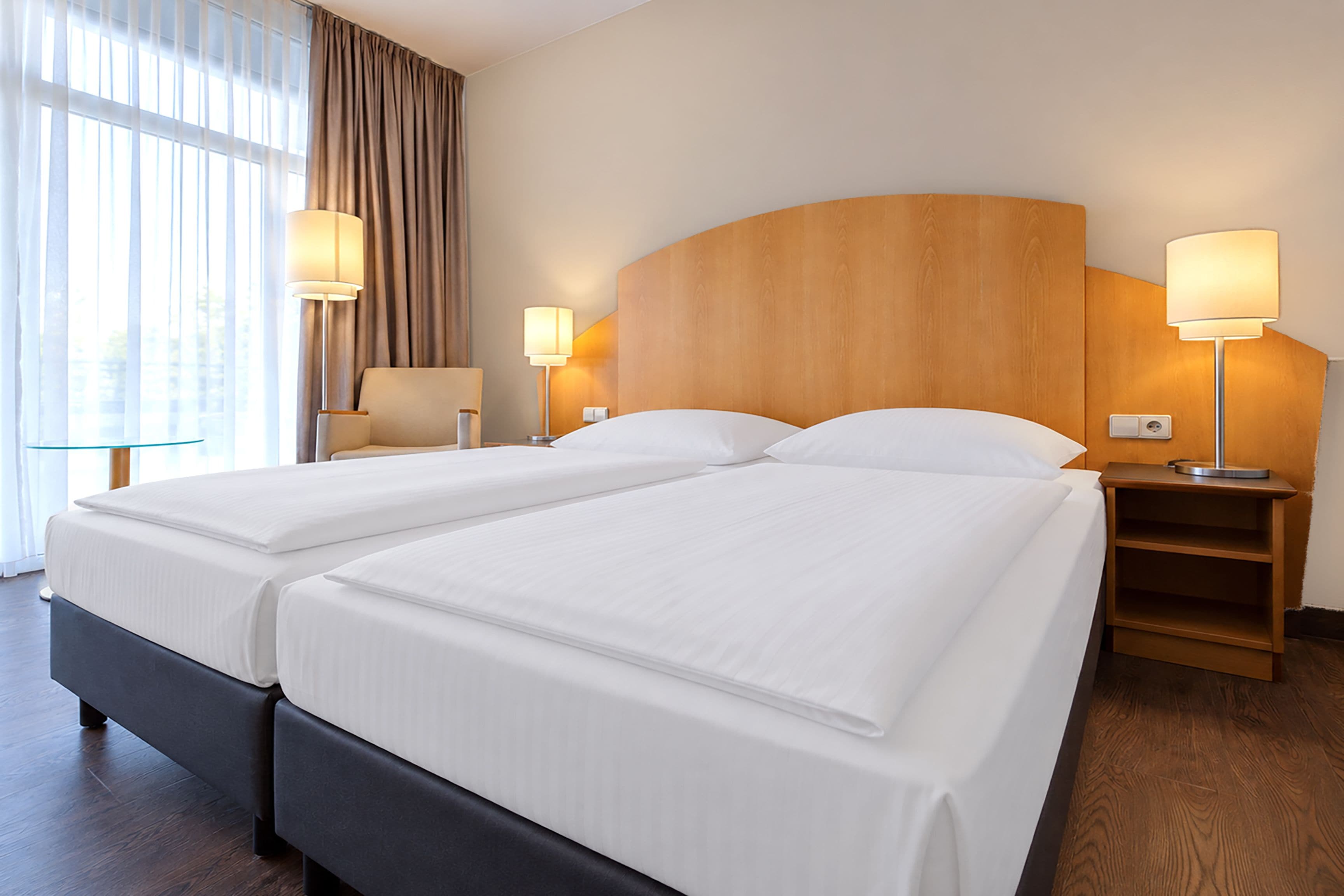A hotel room with a double bed, two bedside tables, a chair, and a large window with curtains.