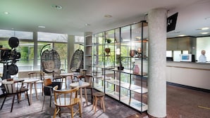 Un hall d’hôtel moderne doté d’espaces aménagés avec des sièges, d’un comptoir d’accueil et de grandes fenêtres offrant une vue sur l’extérieur.