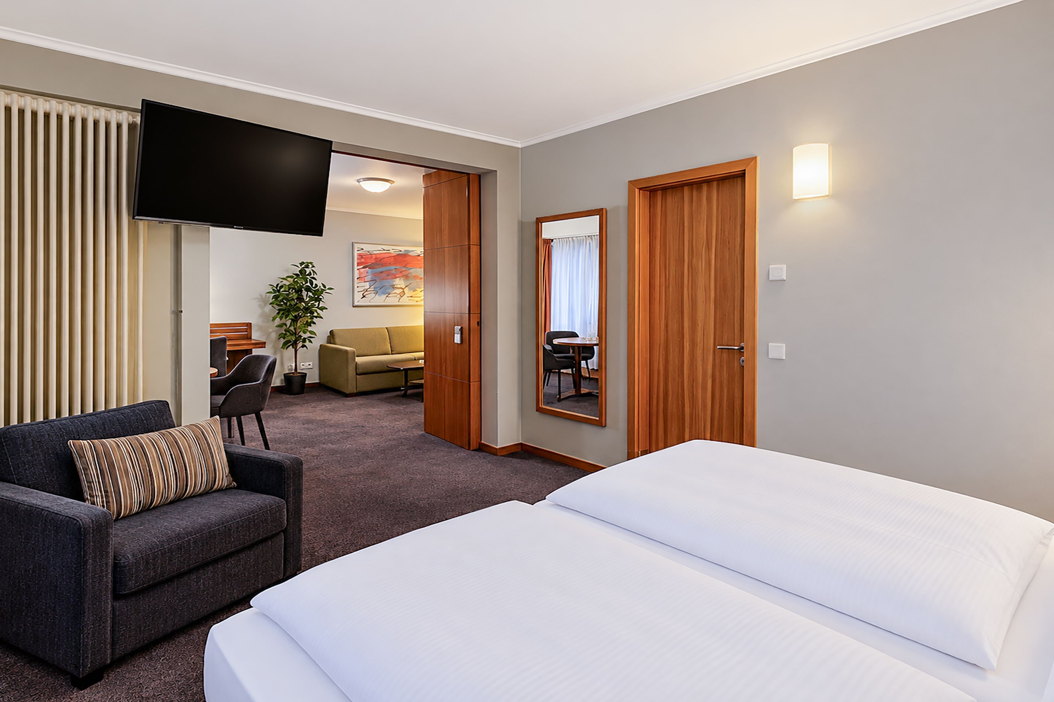 Una habitación de hotel con una cama, un sofá, un televisor y una zona de comedor al fondo.
