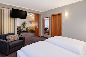 Una habitación de hotel con una cama, un sofá, un televisor y una zona de comedor al fondo.