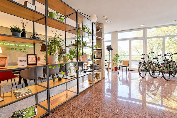 Un espacio de oficina moderno con pared de vidrio, estanterías metálicas con plantas, un escritorio con computadora y bicicletas.