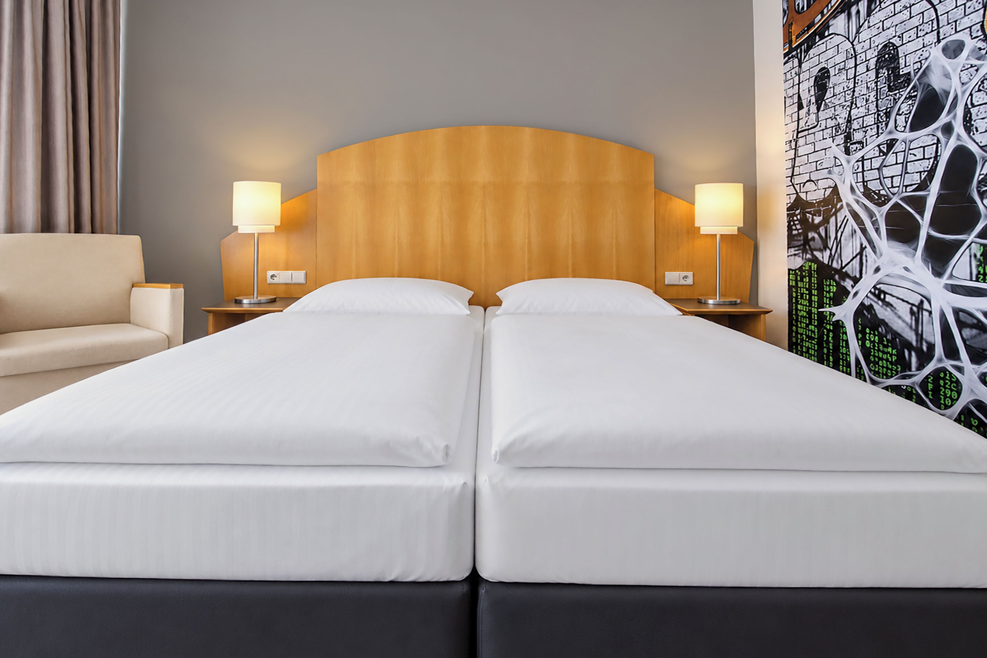 A double bed with a wooden headboard, two bedside tables with lamps, a beige sofa, and a wall with a brick pattern.