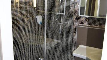 Een douche met een glazen deur, een betegelde muur en een klein wastafeltje met spiegel.