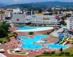 A large swimming pool complex with multiple pools and slides, surrounded by urban buildings and a clear sky. - Hotel Hollywood (Sarajevo)