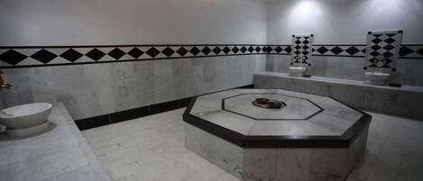 Un baño moderno con un lavamanos hexagonal central, una bañera grande y un área de inodoros separada.