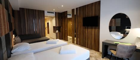Quarto de hotel moderno com cama, escrivaninha, cadeira, televisão e espelho.