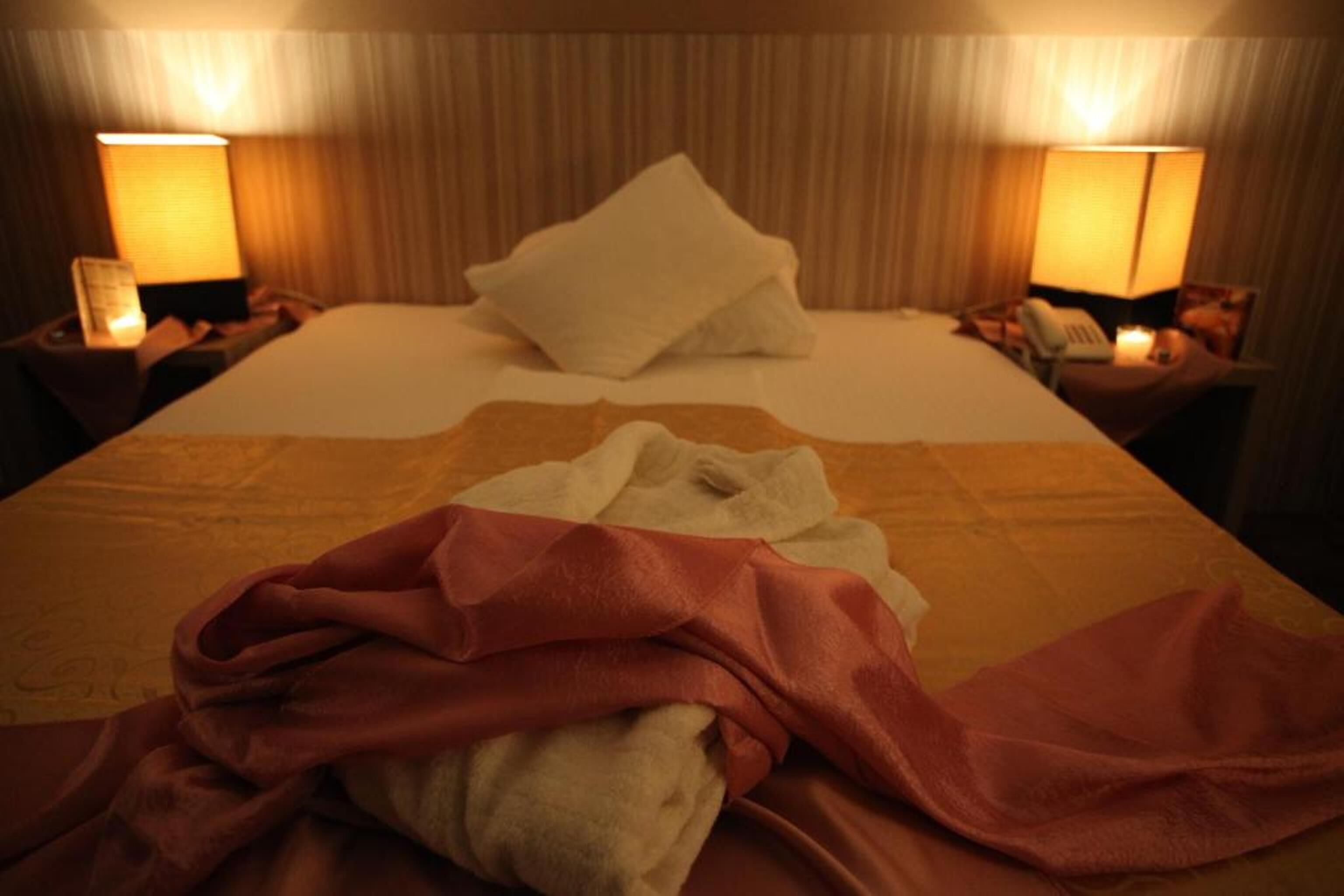 Quarto de hotel com uma cama, duas luminárias laterais e uma mesinha de cabeceira com telefone.
