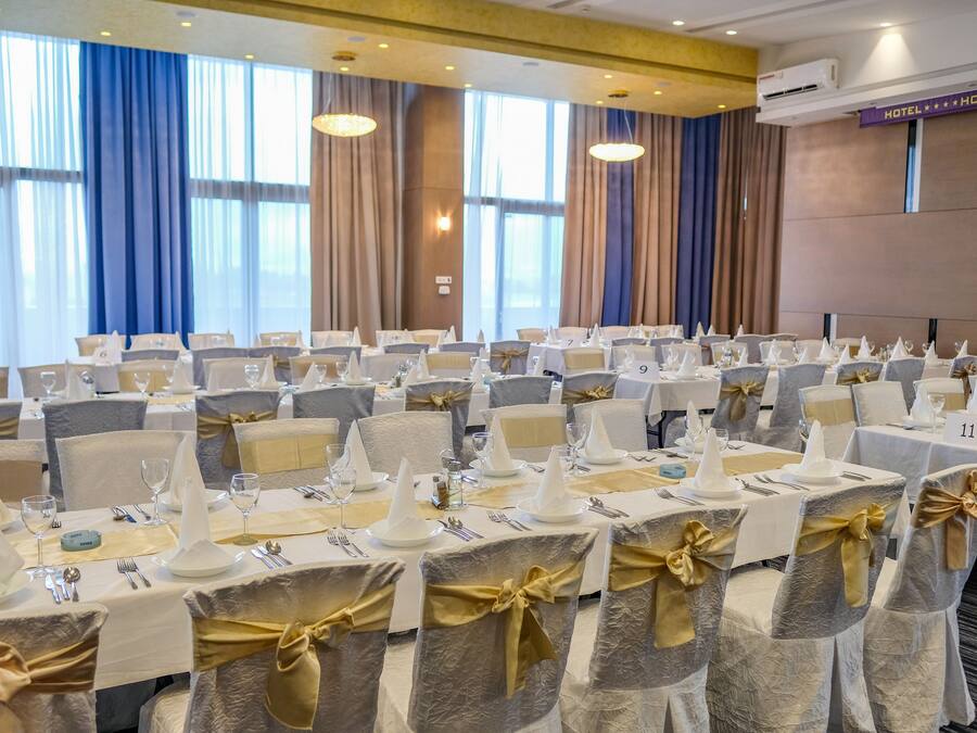 Un salón de banquetes con mesas redondas dispuestas para un evento formal, con manteles blancos, fajas doradas y tarjetas de lugar numeradas.