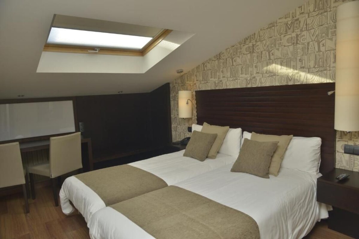 Een hotelkamer met een groot bed, een bureau, een stoel, een lamp en een dakvenster.