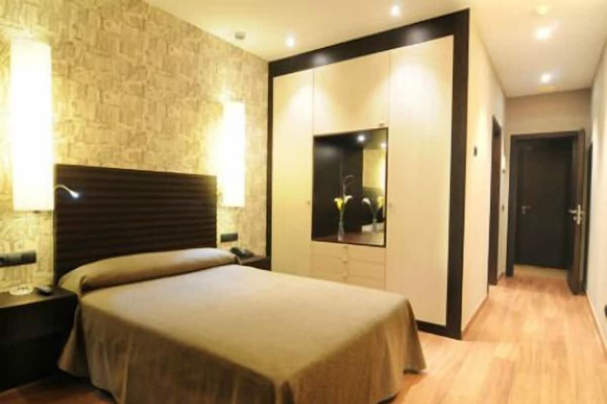 Een hotelkamer met een bed, nachtkastje, spiegel en een houten vloer.