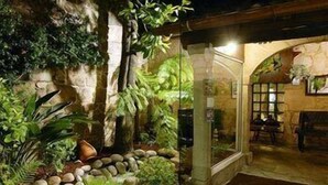 Een helder verlichte ingang met een glazen deur, omgeven door een tuin met diverse planten en een stenen muur.
