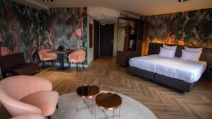 A hotel room with a large bed, two round tables, a sofa, and a decorative wall mural. - Greenside (De Koog)