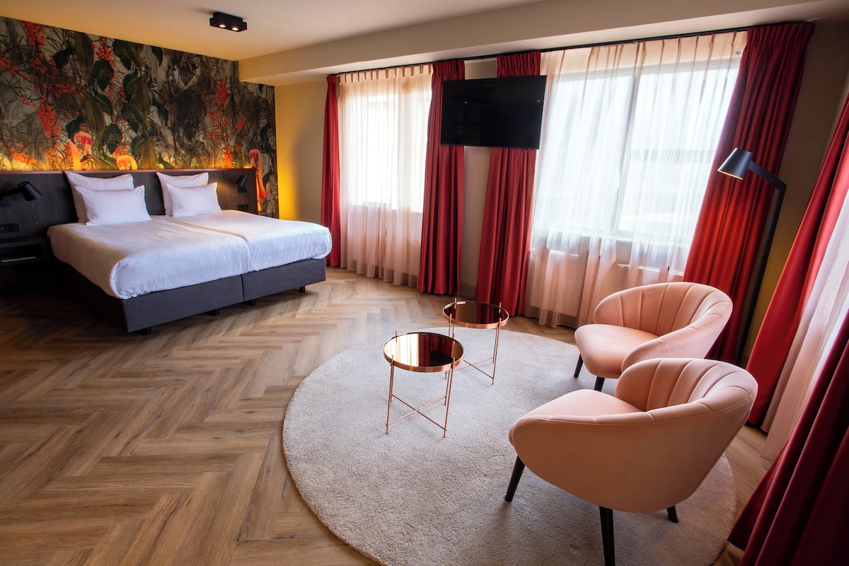 A hotel room with a large bed, two armchairs, a round coffee table, and a TV mounted on the wall.