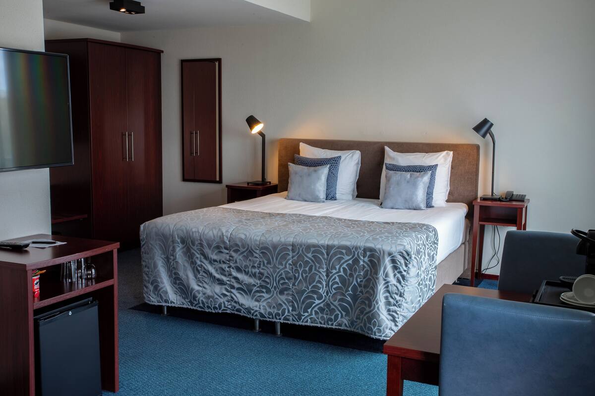 A hotel room with a large bed, two bedside lamps, a TV, a desk with a computer, and a wardrobe.