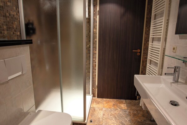 Un baño con cabina de ducha de vidrio, un lavabo blanco y una puerta de madera oscura.