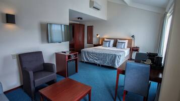 A hotel room with a bed, a desk, a chair, a TV, and a small kitchenette.
